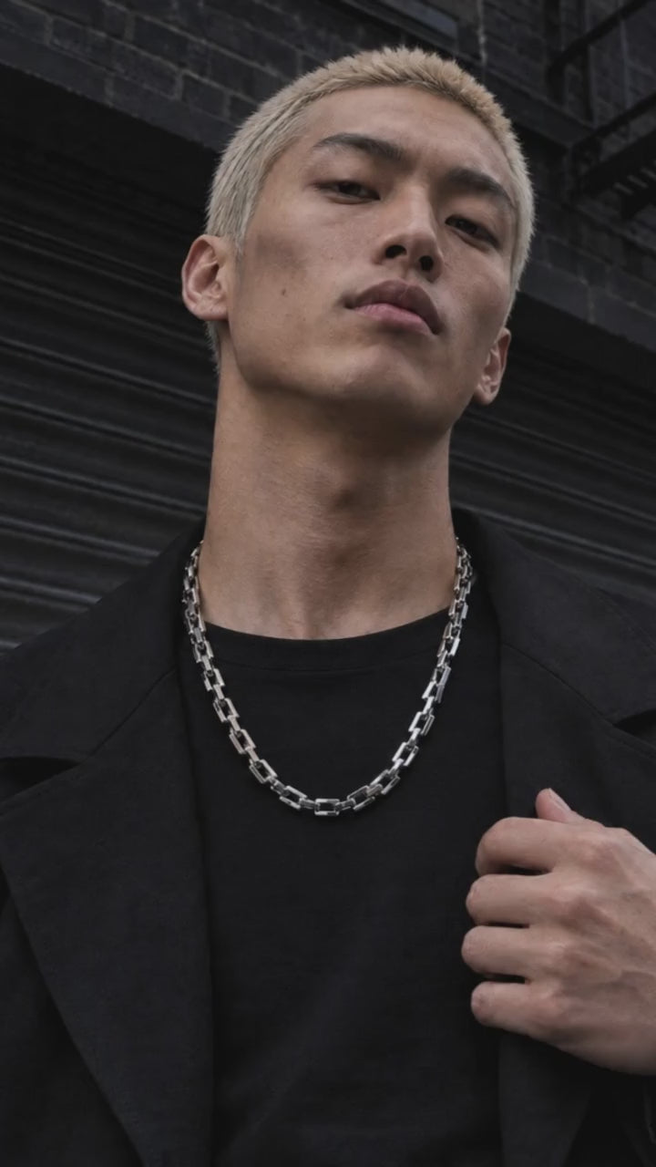 Tartarus necklace showcased by an adult male model in black crew-neck streetwear, with a moving close-up of the silver design.