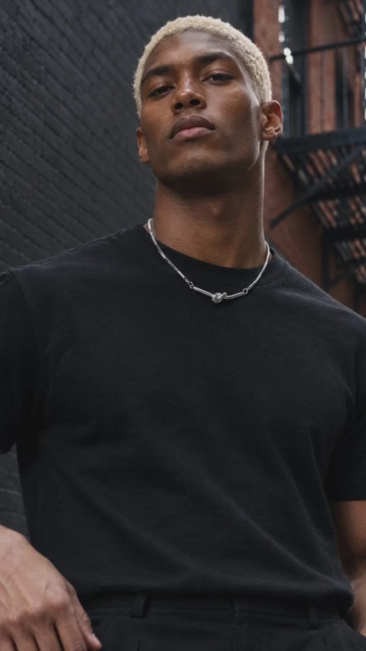 Ophion necklace showcased by an adult male model in black crew-neck streetwear, with a moving close-up of the silver design.