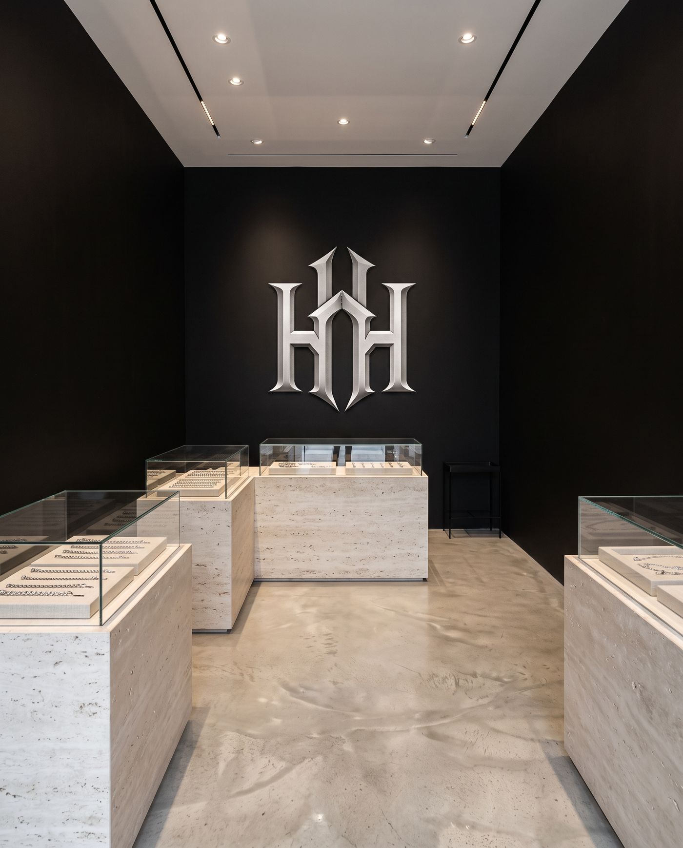 Black room with travertine display cases and a silver HH monogram